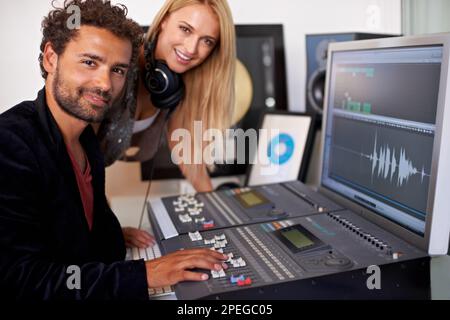 Their business is sound. Two young audio engineers working on a mixing desk and smiling at the camera. Stock Photo