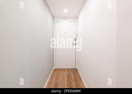 View of the front door in a white narrow empty corridor in a hotel or small apartment for one person. Concept of compact rooms for a young couple or a Stock Photo
