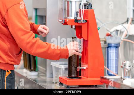 capping beer bottles on a machine in a brewery Stock Photo
