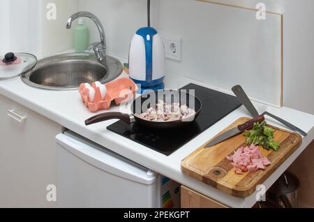 Cooking scrambled eggs with ham. Frying onions in a pan Stock Photo