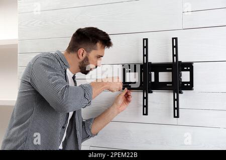 Man with screwdriver installing TV bracket on wall indoors Stock Photo