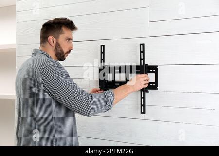 Man installing TV bracket on wall indoors Stock Photo