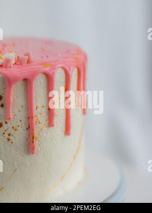 pink frosted dripping icing white birthday cake cake with unicorn , meringue and sprinkles toppers, golden edible paint brush strokes on stand Stock Photo