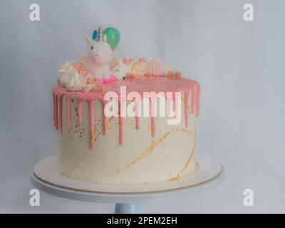 pink frosted dripping icing white birthday cake cake with unicorn , meringue and sprinkles toppers, golden edible paint brush strokes on stand Stock Photo