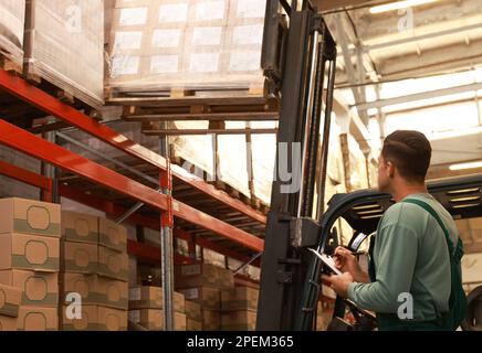 Worker near forklift truck with cardboard boxes in warehouse. Logistics ...