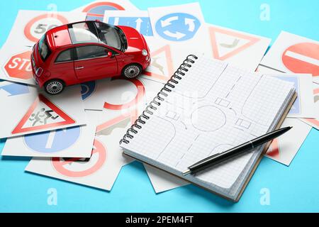 Many different road sign cards, notebook with sketch of roundabout and toy car on light blue background. Driving school Stock Photo