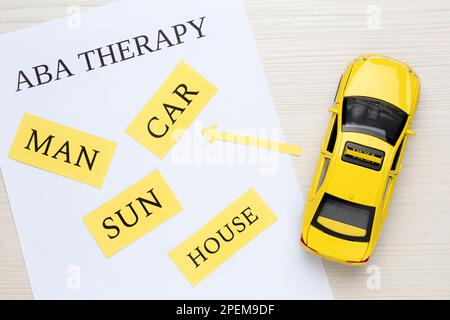 Taxi car model near sheet of paper with text ABA Therapy and different words on white wooden table, flat lay. Applied behavior analysis Stock Photo