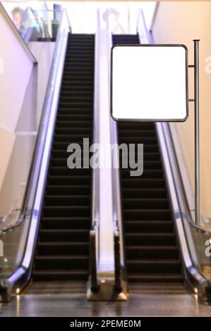 Blank advertising board near escalators in shopping mall. Space for text Stock Photo