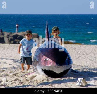 Life-sized sculpture of shark on beach (by Desthureson, 2011) at Swell sculpture Festival, Gold Coast Australia. Accompanied by 2 admirers. Sand, sea. Stock Photo