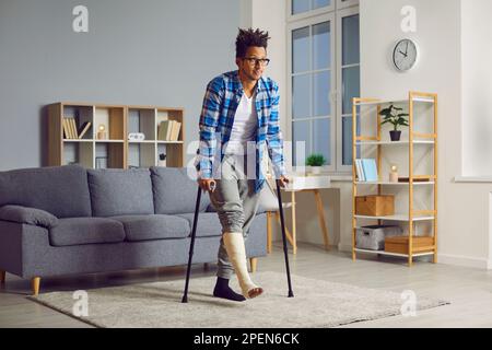 Handicapped young african man with broken leg trying to walk with crutches. Stock Photo