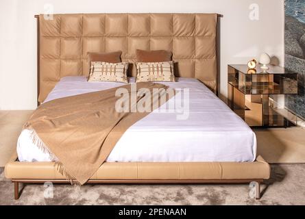 Double bed with soft leather headboard and wool throw in pastel beige tones. Stock Photo