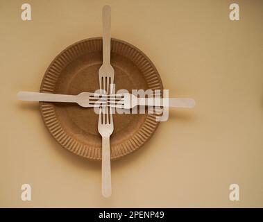 Four cross-shaped wooden forks on a brown paper plate, top view. Healthy eating without treatment Stock Photo