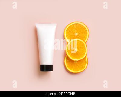 Bottle for branding and label. Mockup of pink squeeze bottle cream tube with black cap and orange slices on light pink background. Top view. Natural o Stock Photo