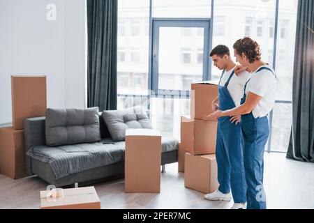 Two young movers in blue uniform working indoors in the room Stock Photo