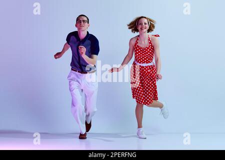 Beautiful girl and man in colorful costumes dancing retro style dances against gradient blue purple studio background Stock Photo