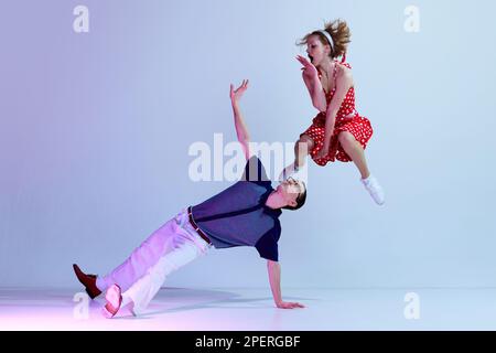 Jumping. Beautiful girl and man in colorful costumes dancing retro style dances against gradient blue purple studio background Stock Photo