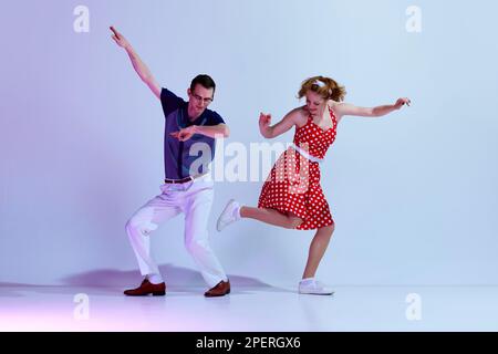 Stylish girl and man in colorful costumes dancing retro style dances against gradient blue purple studio background Stock Photo