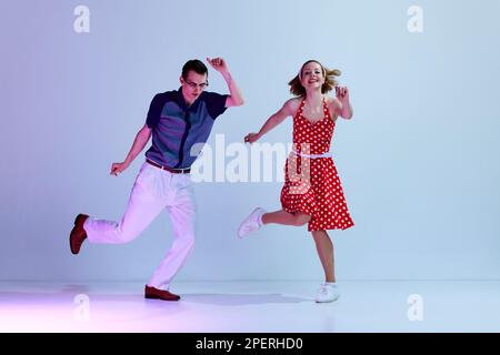 Happy mood. Beautiful girl and man in colorful costumes dancing retro style dances against gradient blue purple studio background Stock Photo