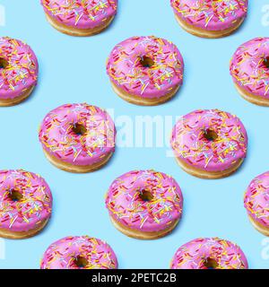 Bright flat lay seamless pattern with donuts. Pink glazed donuts with colorful sugar sprinkles on blue background. Stock Photo