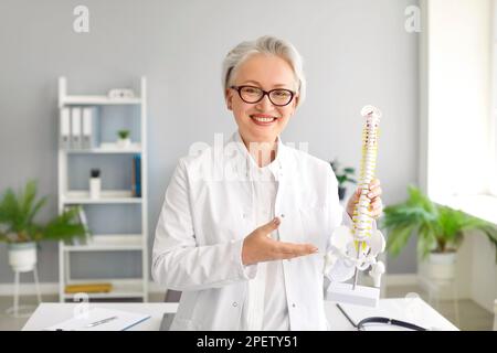 Portrait of happy female doctor holding anatomical model of human spine and smiling Stock Photo