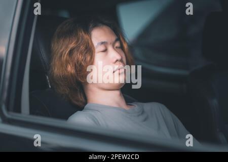 Young asian man with long hair sleeping in his car. Stock Photo