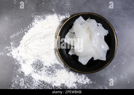 Flat white big noodles in a black plate surrounded by all-purpose flour. on a dark background, Uncooked Stock Photo