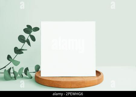 Blank Greeting Card, Invitation Mockup. Front view Eucalyptus Plant, Modern Wooden Plate, Boho Paper Mock Up on Green Table Copy Space. Minimal Busine Stock Photo