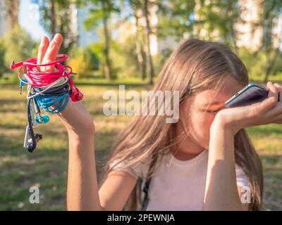 Girl with the phone in one hand and four pairs of in-ear wired colorful pink, blue, white, and black earbuds tangled around the other hand. Messy wire Stock Photo