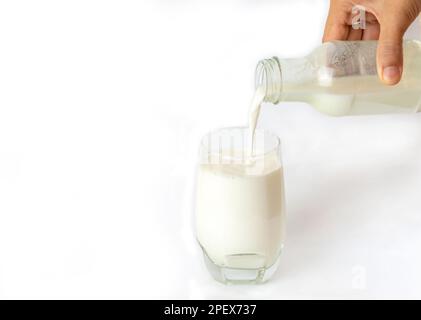 Close up hand hold bottle pouring milk to glass on isolate white background. Stock Photo