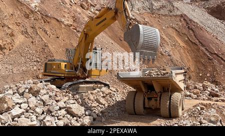 Excavator Working On Huge Mining Site, Loading The Trucks, Trucks Transport The Material. Stock Photo