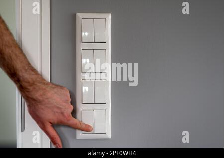 Row of eight light switches, while a finger switches on one light switch. Stock Photo