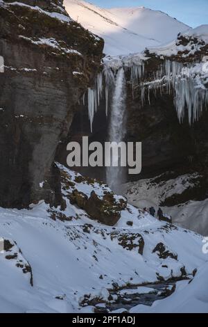 Group of mountaineering tourists on a route through a completely snow covered path between with the Seljalandsfoss waterfall in front of them and with Stock Photo