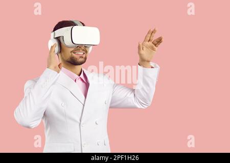 Smiling young smart man wearing virtual reality goggles isolated on pastel pink background. Stock Photo