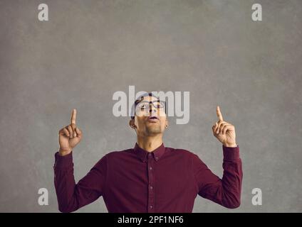 Surprised young black man pointing with both fingers at something on copy space above Stock Photo