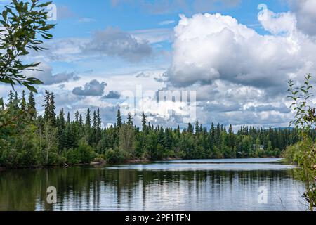 Fairbanks, Alaska, USA - July 27, 2011: Blue cloudscape over Chena River landscape with green forest belt between water and sky Stock Photo