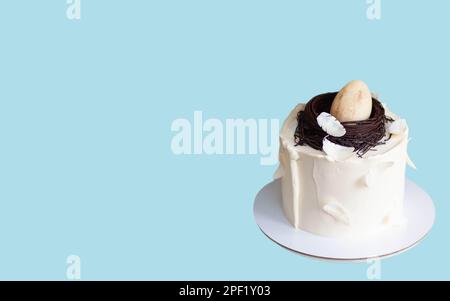 Elegant easter cake decorated with chocolate bird's nest, egg and feathers. Blue background with copy space. Horizontal orientation Stock Photo