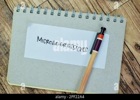 Concept of Microaggressions write on sticky notes isolated on Wooden Table. Stock Photo