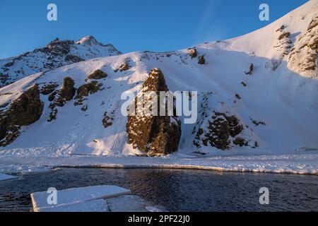 Frozen chunks of ice floating down frozen river flowing from Iceland's Skógafoss waterfall illuminated by late afternoon sunlight. Stock Photo