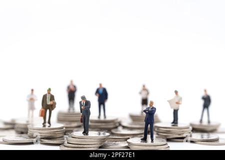 Business amd Money Concept. Group of businessman miniature figures people standing on stack of silver coin on white background. Stock Photo