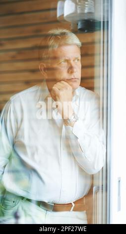Taking a moment to think it over...a contemplative senior man looking out from his bedroom window. Stock Photo