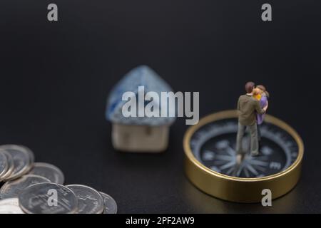 Money, Financial, Business and Family concept, Miniature figures man, woman and child stand on compass with mini house toy model and pile of silver co Stock Photo