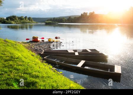 Orange and yellow packrafts rubber boats on a sunrise river near old wooden boats. Packrafting and active lifestile concept Stock Photo