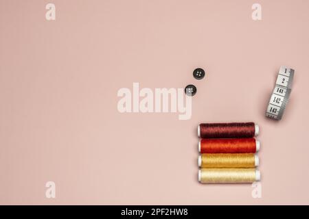 Still life with colored threads with black buttons and tape measure on a plain pink background Stock Photo