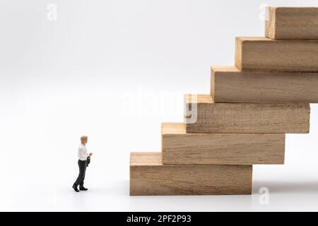 Business and Planning Concept. Businessman miniature figure people walking to stack of wooden block toy on white background. Stock Photo