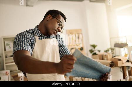 African american designer making a phone call, looking at fabric. Young tailor using his cellphone while looking at material. Creative seamstress Stock Photo