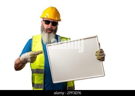Construction worker with beard and sunglasses pointing his finger at a blank blackboard, isolated on white background. Stock Photo
