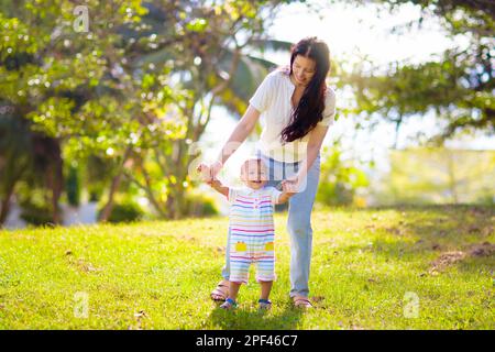 Mother and son in sunny park. Loving Asian family playing outdoor. Mom holding little baby boy. Young woman and adorable child play and laugh. Stock Photo