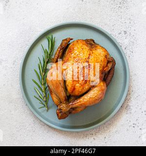 Whole baked (fried) chicken in spices with rosemary on a dish on  light background. Festive food for thanksgiving, birthday. Fast food, top view. Stock Photo