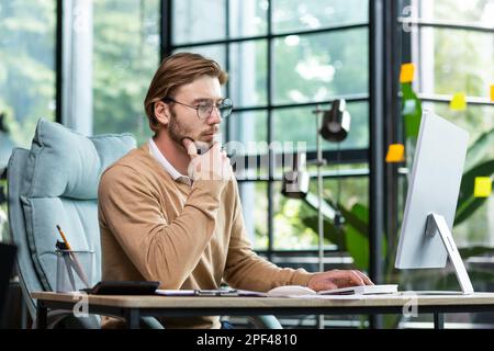A young male businessman is concentrating on working from a home office at a computer. Stock Photo