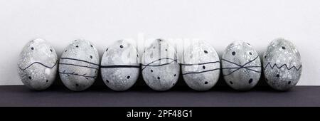 Seven grey Easter eggs in a black pattern on a grey background. Happy Easter concept. Banner Stock Photo